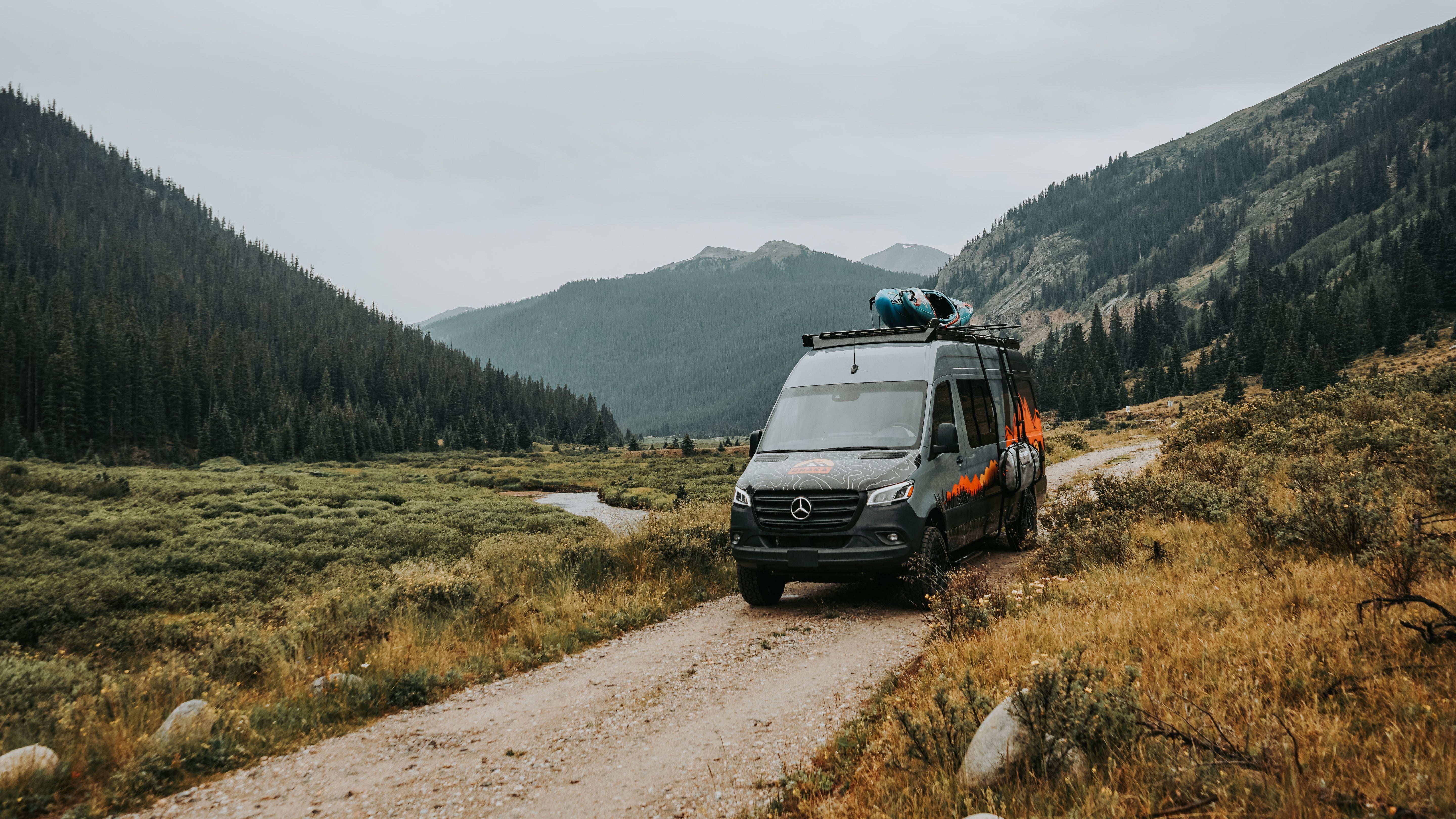 Sprinter Van with Unaka roof rack and surfboard on a mountain road